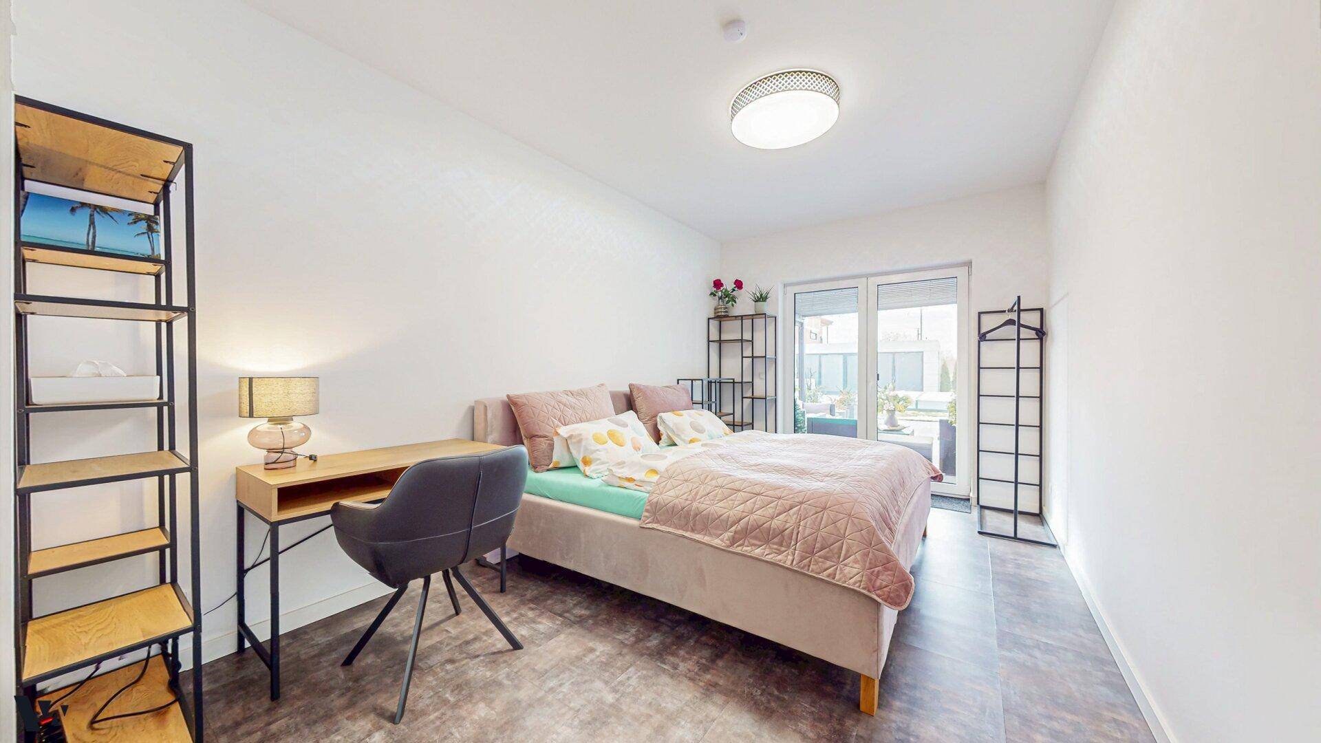 Helles Schlafzimmer mit Doppelbett, Schreibtisch und Zugang zu einem kleinen Außenbereich.