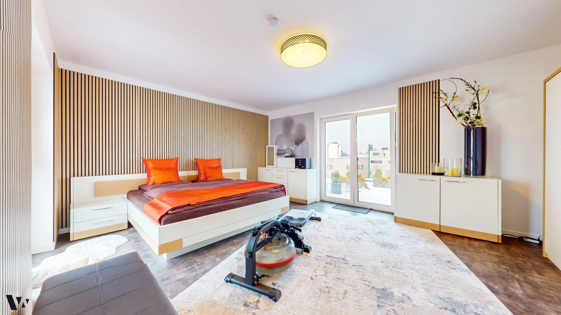 Geräumiges Schlafzimmer mit Doppelbett, Holzakzenten und Zugang zu einem Balkon oder einer Terrasse.