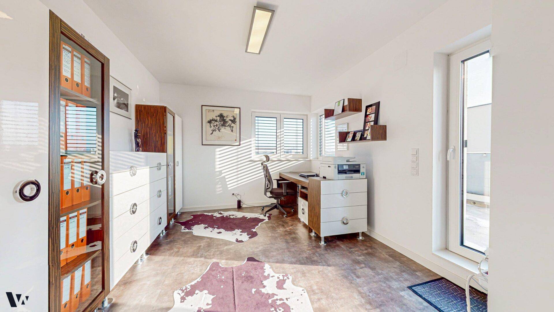 Helles Arbeitszimmer mit Schreibtisch, Regalen und großen Fenstern für viel Tageslicht.