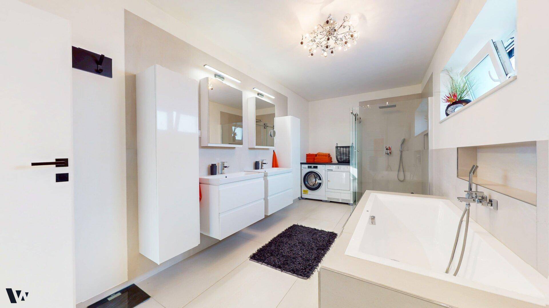 Großes, modernes Badezimmer mit Badewanne, Doppelwaschbecken und Waschmaschine.