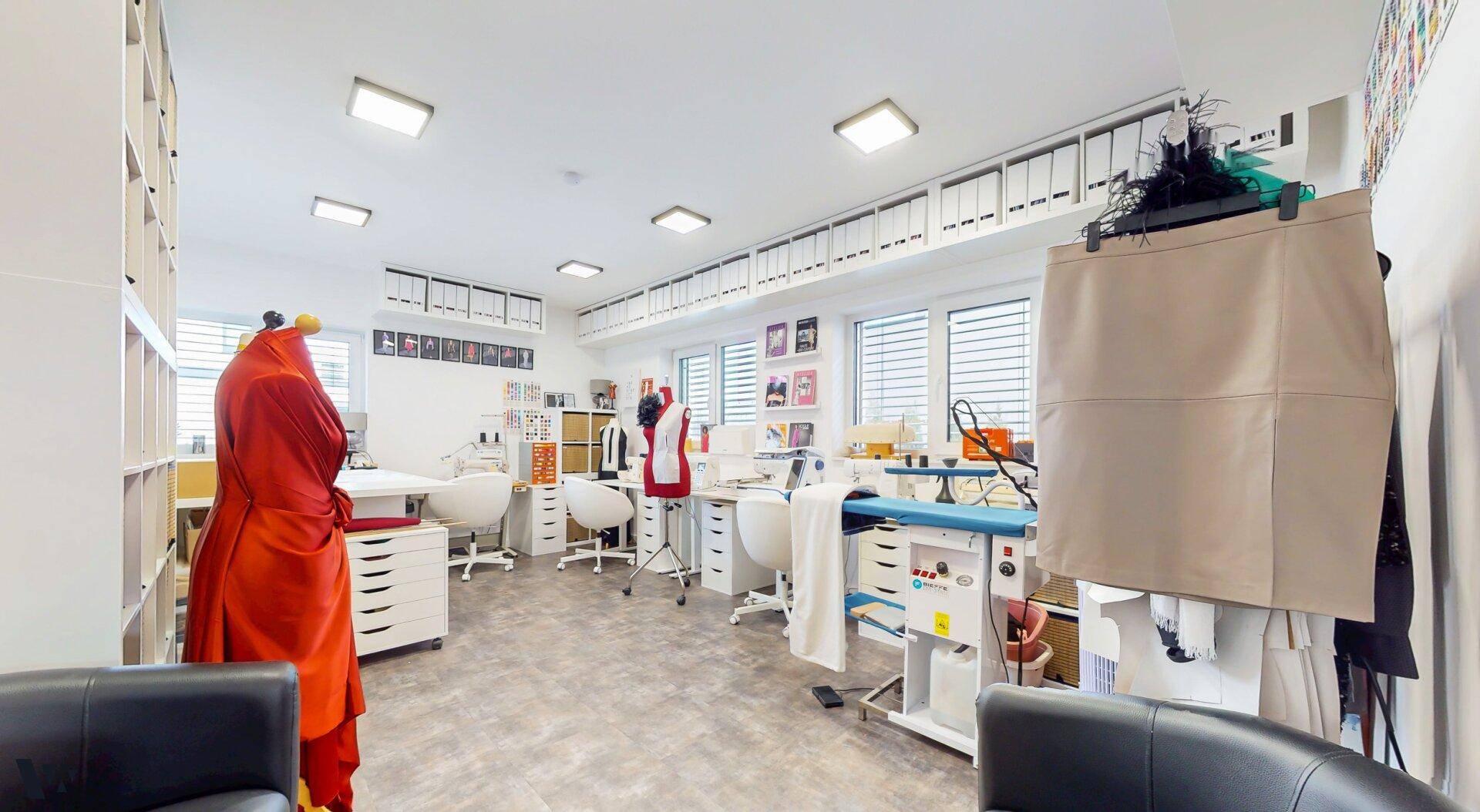 Helles Atelier mit mehreren Arbeitsplätzen, Nähmaschinen und großen Fenstern.