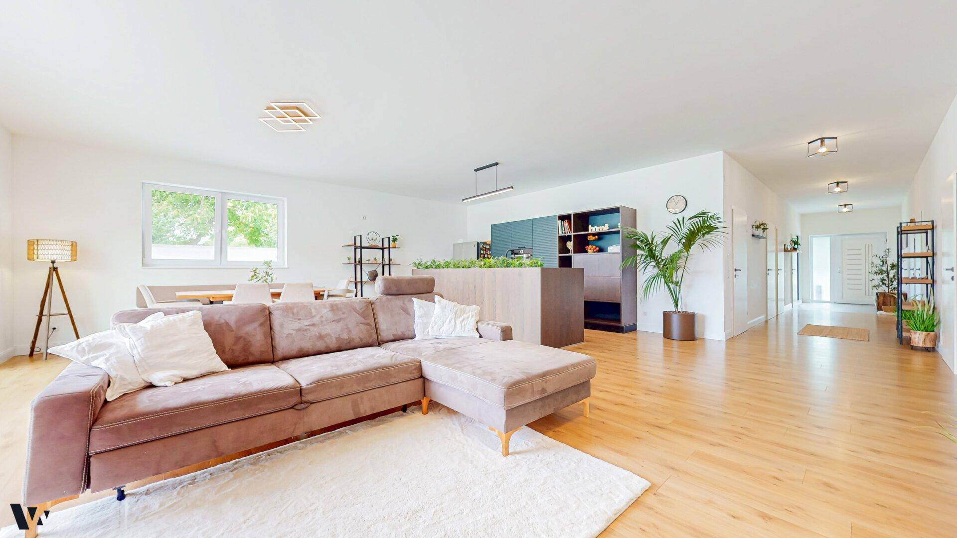 Geräumiger Wohnbereich mit bequemer Couch, Holzboden und offener Verbindung zur Küche.