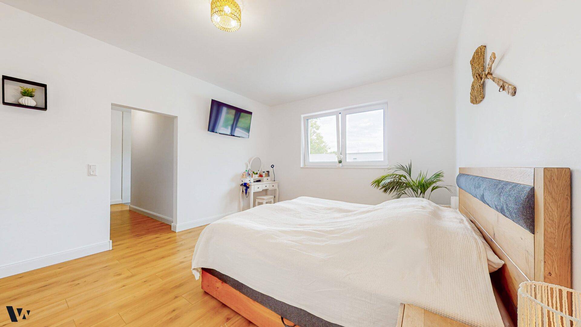 Helles Schlafzimmer mit Holzboden, Doppelbett und Fenster mit Blick ins Grüne.