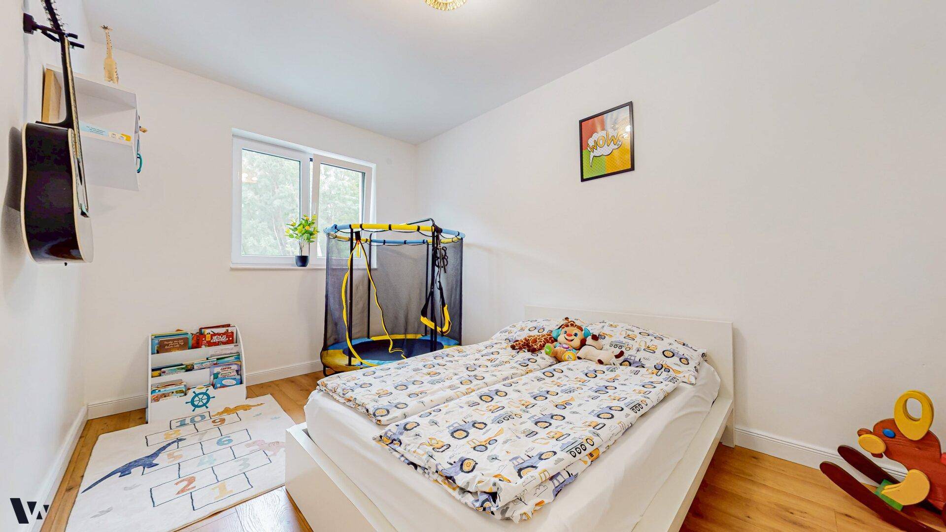 Helles Kinderzimmer mit Einzelbett, kleinem Trampolin und Holzboden.