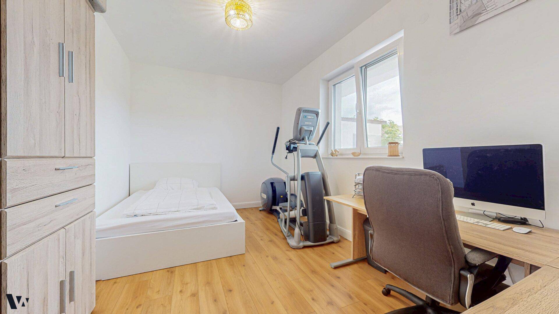 Arbeitszimmer mit Schreibtisch, Einzelbett und Fitnessgerät, vielseitig nutzbar.