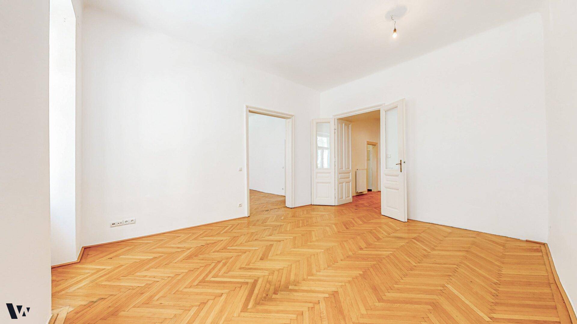 Großes, helles Zimmer mit Fischgrätparkett und mehreren Türen zu angrenzenden Räumen.