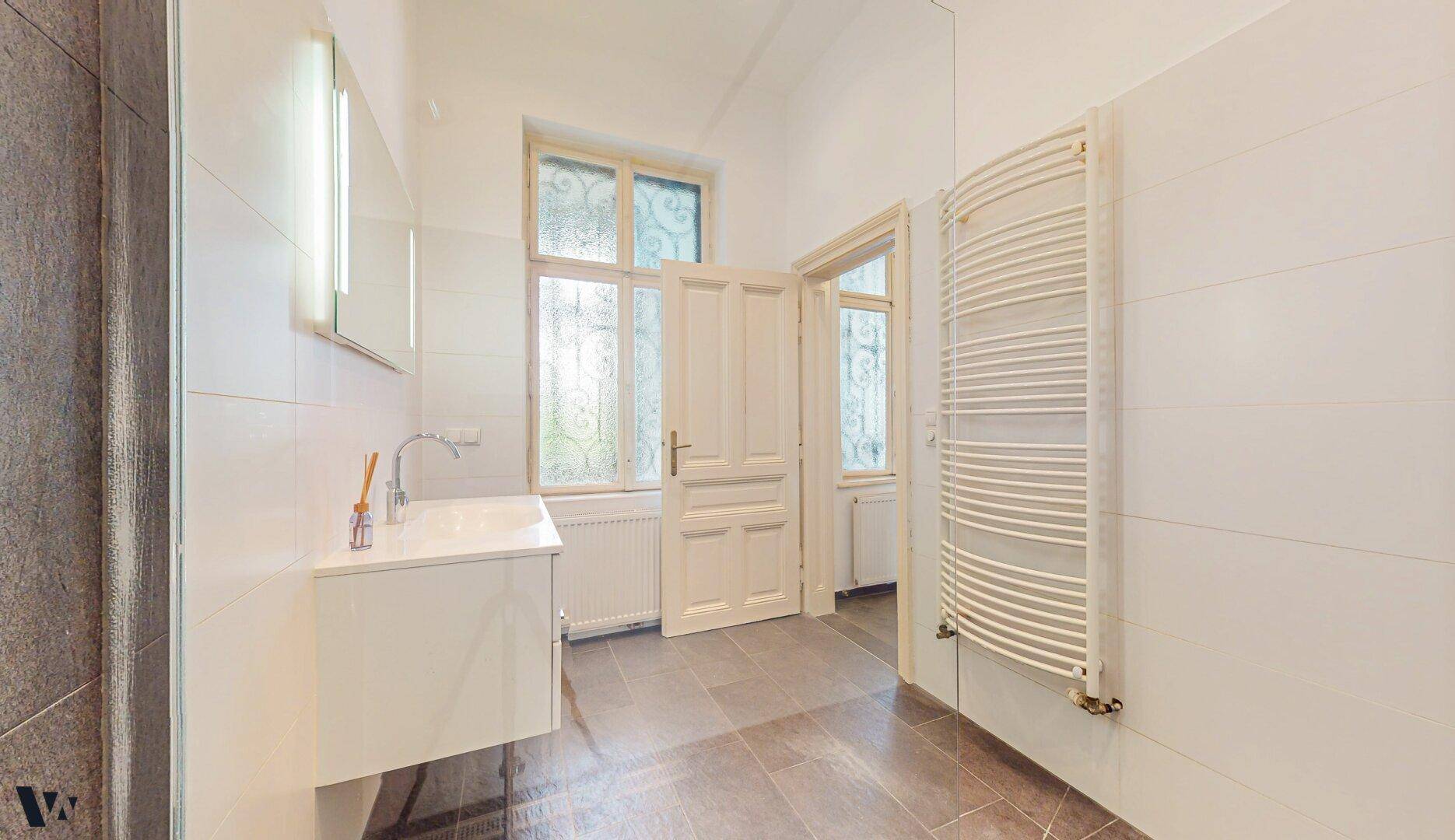 Geräumiges Badezimmer mit modernem Waschtisch, Fenster und Handtuchheizkörper.