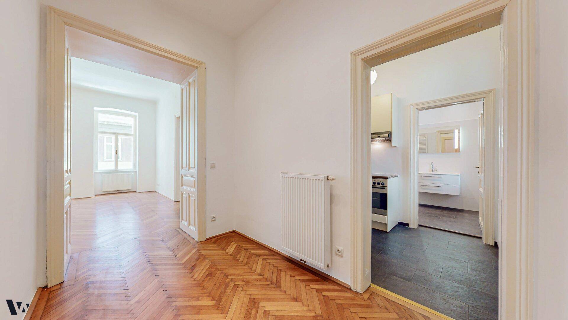 Heller Flur mit Fischgrätparkett, der zu Wohnzimmer, Küche und Bad führt.