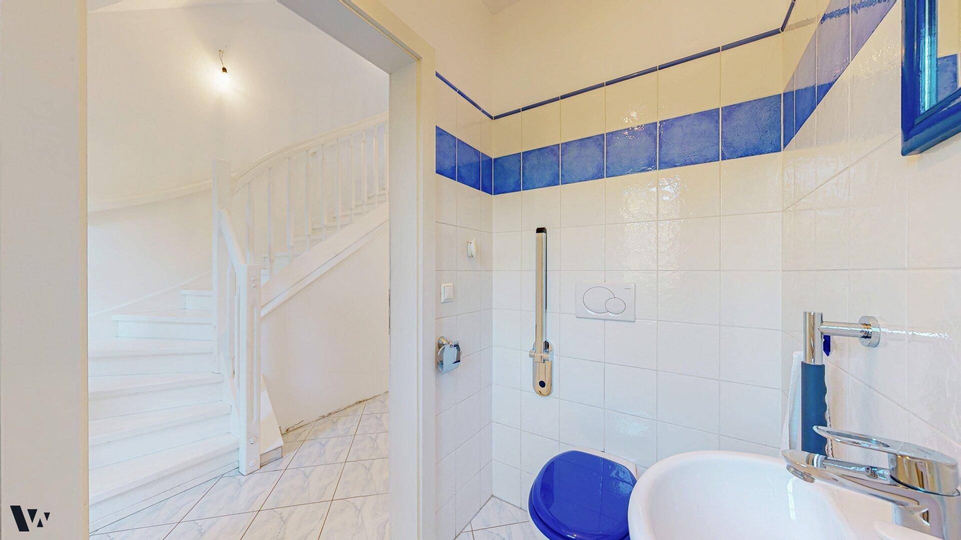 Gäste-WC mit blauen Akzentfliesen, Waschbecken und Toilette, vom Flur aus zugänglich.