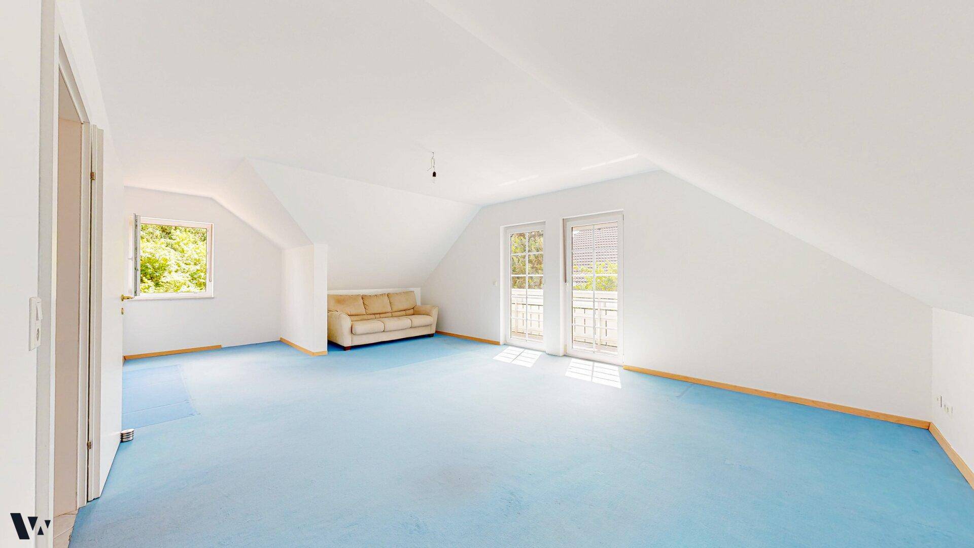 Geräumiges Dachgeschosszimmer mit blauer Auslegware, schrägen Decken und Zugang zu einem französischen Balkon.
