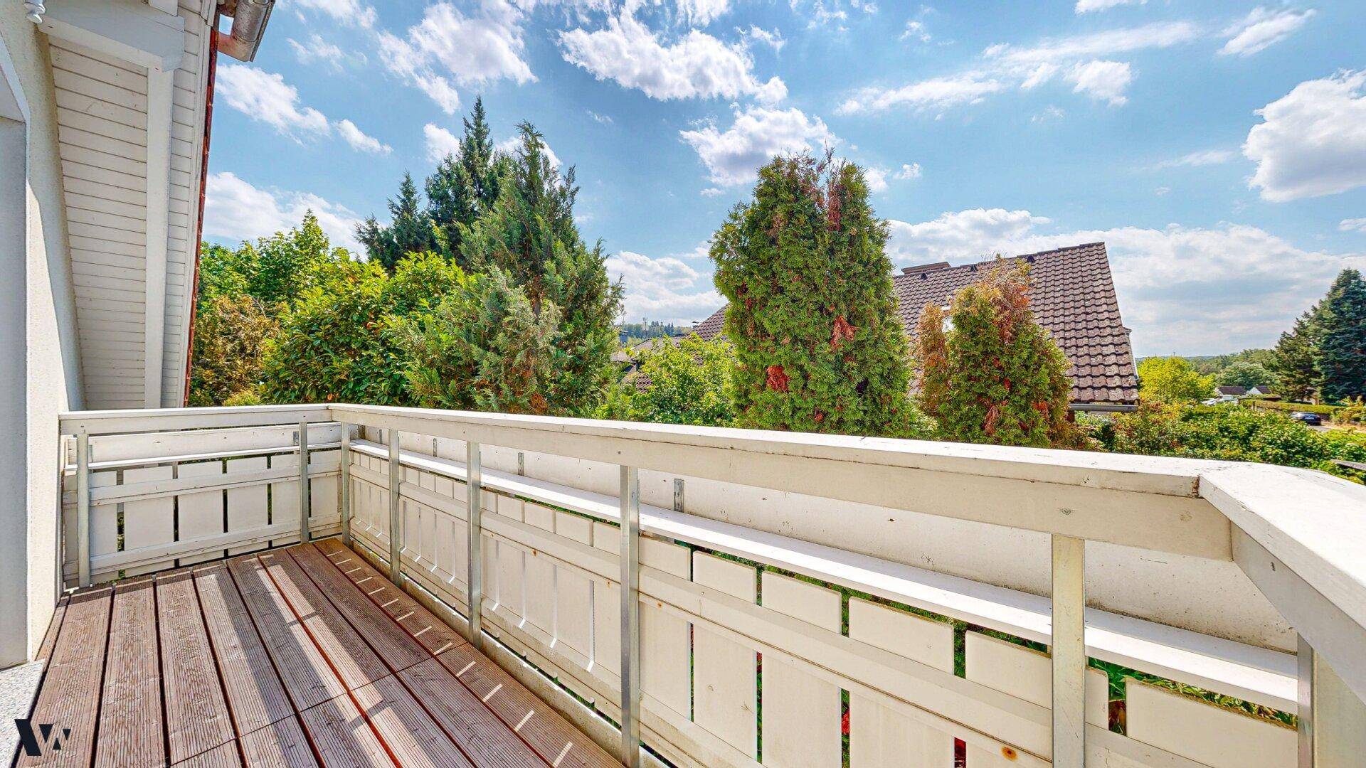 Kleiner Balkon mit Holzboden und weißem Geländer, bietet einen schönen Blick ins Grüne.