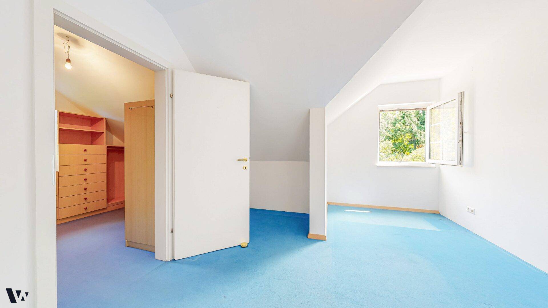 Helles Dachgeschosszimmer mit blauem Teppichboden und angrenzendem begehbarem Kleiderschrank.