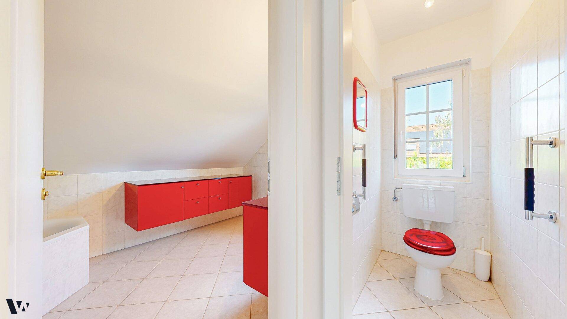 Helles Badezimmer im Dachgeschoss mit roten Möbeln, Fenster und schrägen Wänden.