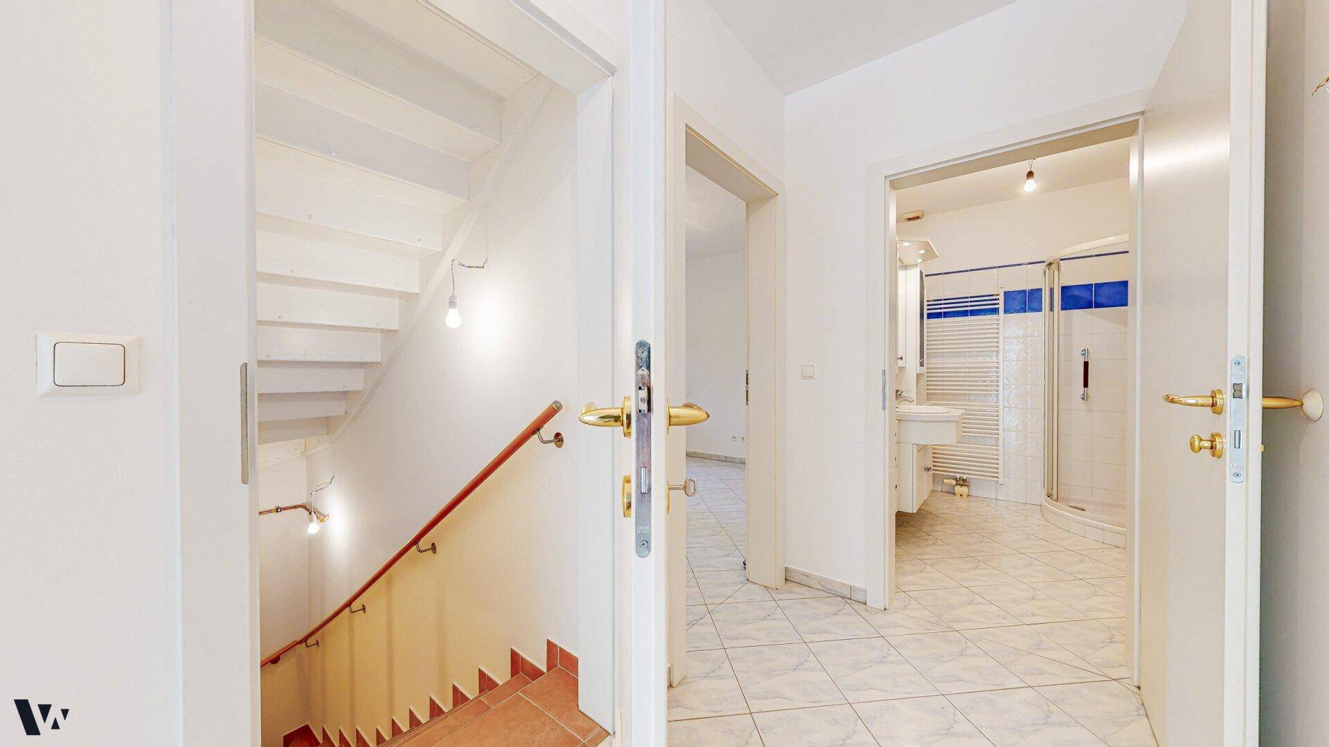 Heller Flur mit Treppenabgang und Blick in ein weiteres Badezimmer mit Dusche.