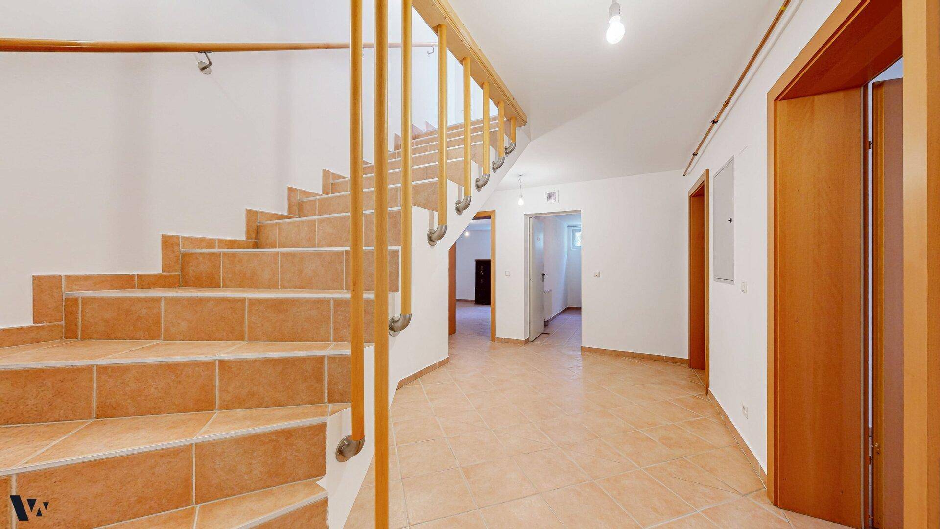 Geräumiger Flur mit gefliester Treppe, Holzgeländer und Zugang zu weiteren Räumen.