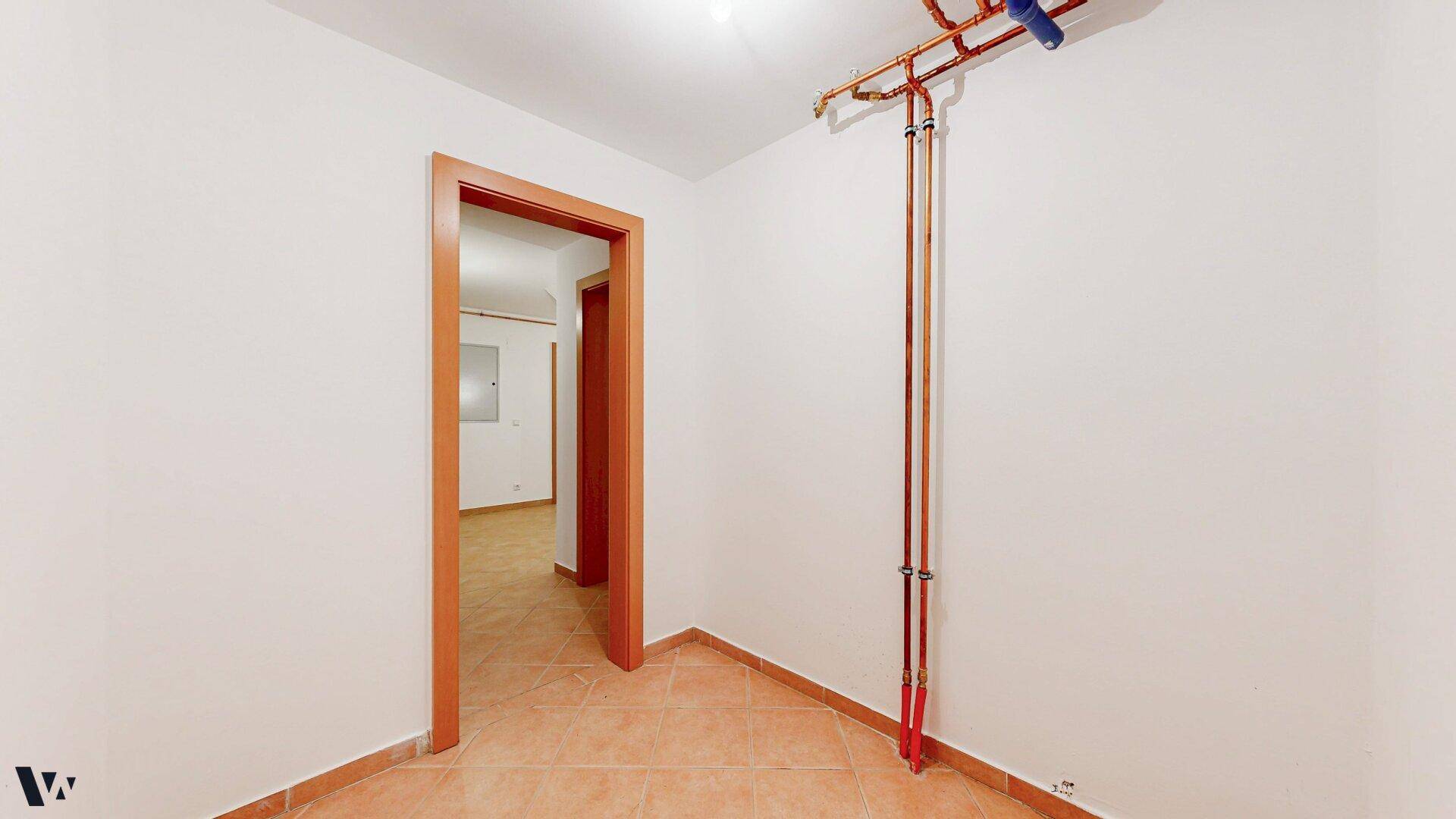Kleiner Raum mit gefliestem Boden und sichtbaren Kupferrohren an der Wand.