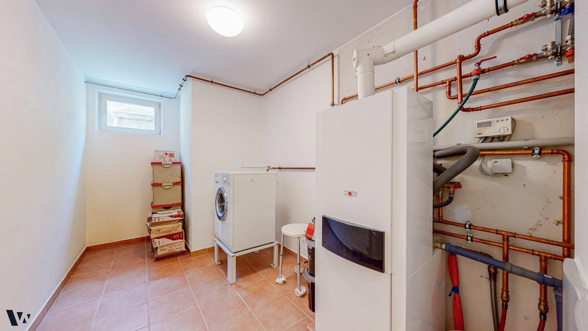 Hauswirtschaftsraum im Keller mit Heizungsanlage, Waschmaschine und kleinem Fenster.