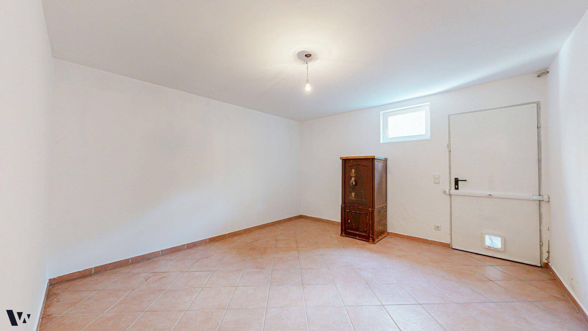 Kellerraum mit gefliestem Boden, kleinem Fenster und einer Tür mit Katzenklappe.