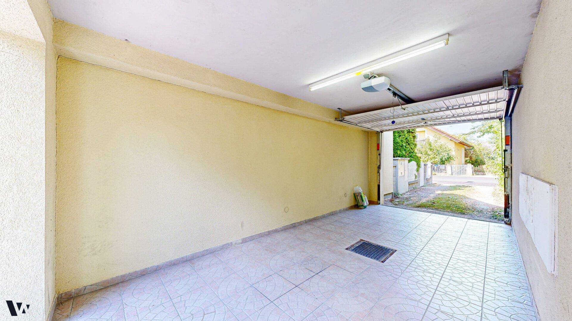 Geräumige Garage mit gefliestem Boden und offenem Tor, bietet Platz für ein Fahrzeug.
