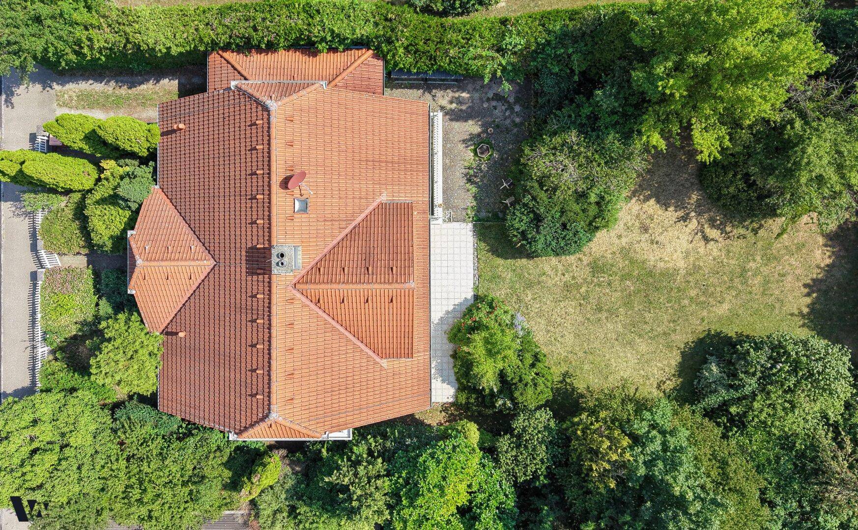 Luftaufnahme des Grundstücks mit dem Haus und seinem roten Ziegeldach, umgeben von viel Grün.
