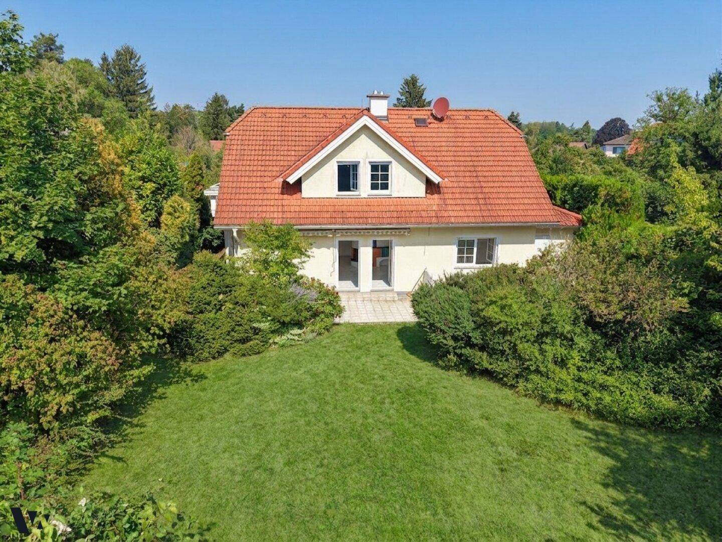 Vogelperspektive des Hauses mit rotem Ziegeldach, umgeben von einem weitläufigen grünen Garten und Bäumen.