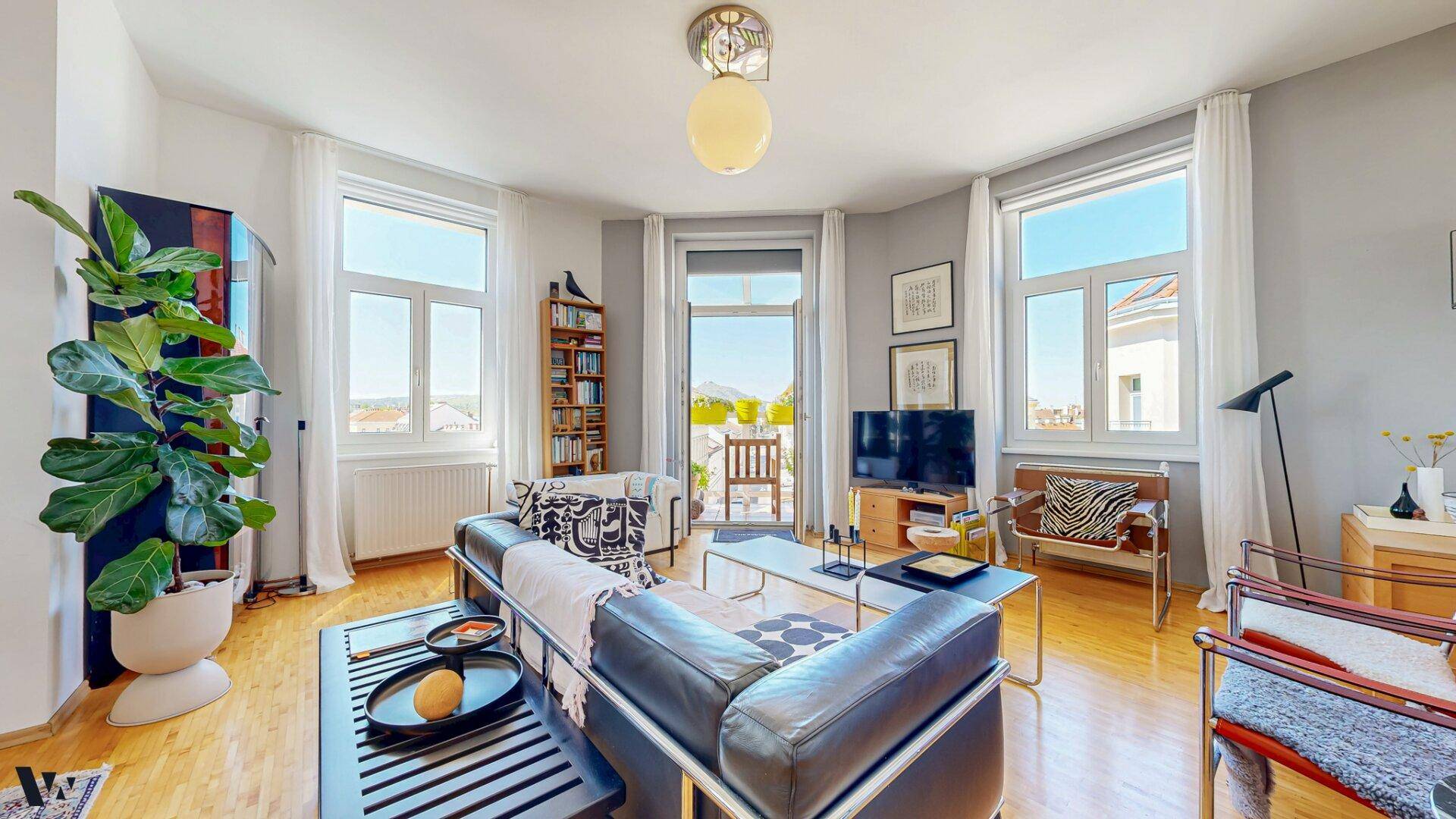 Gemütliches Wohnzimmer mit Ledersofa, Holzboden und Zugang zu einem Balkon, hell und einladend.