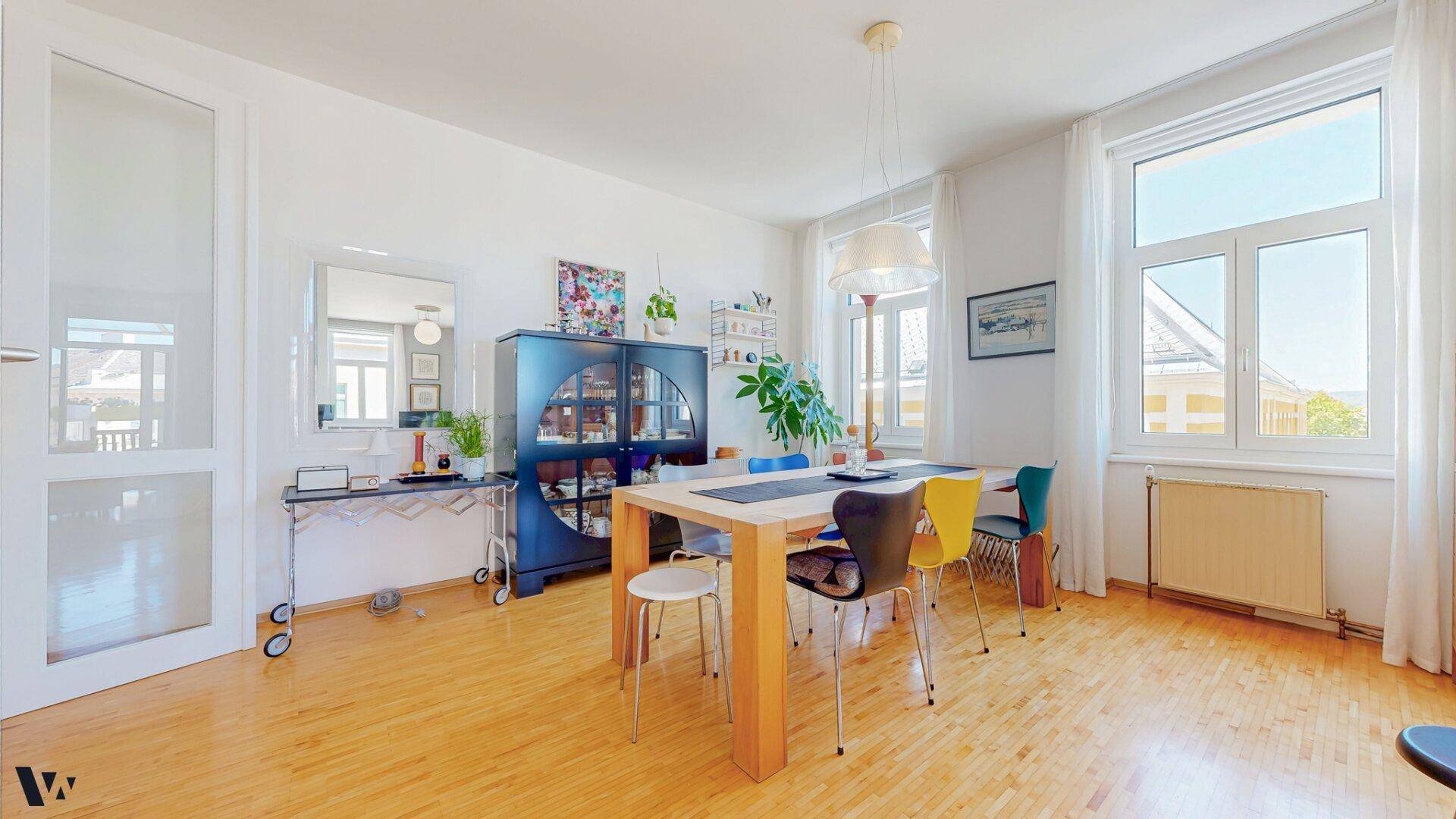 Heller Essbereich mit Holzboden, einem großen Holztisch und bunten Stühlen, ideal für gesellige Runden.