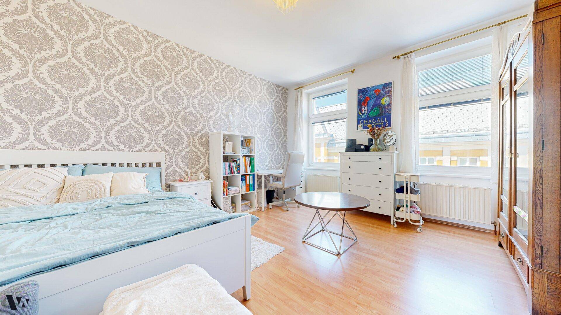 Helles Schlafzimmer mit gemusterter Tapete, Holzboden und einem großen Bett, einladend und komfortabel.