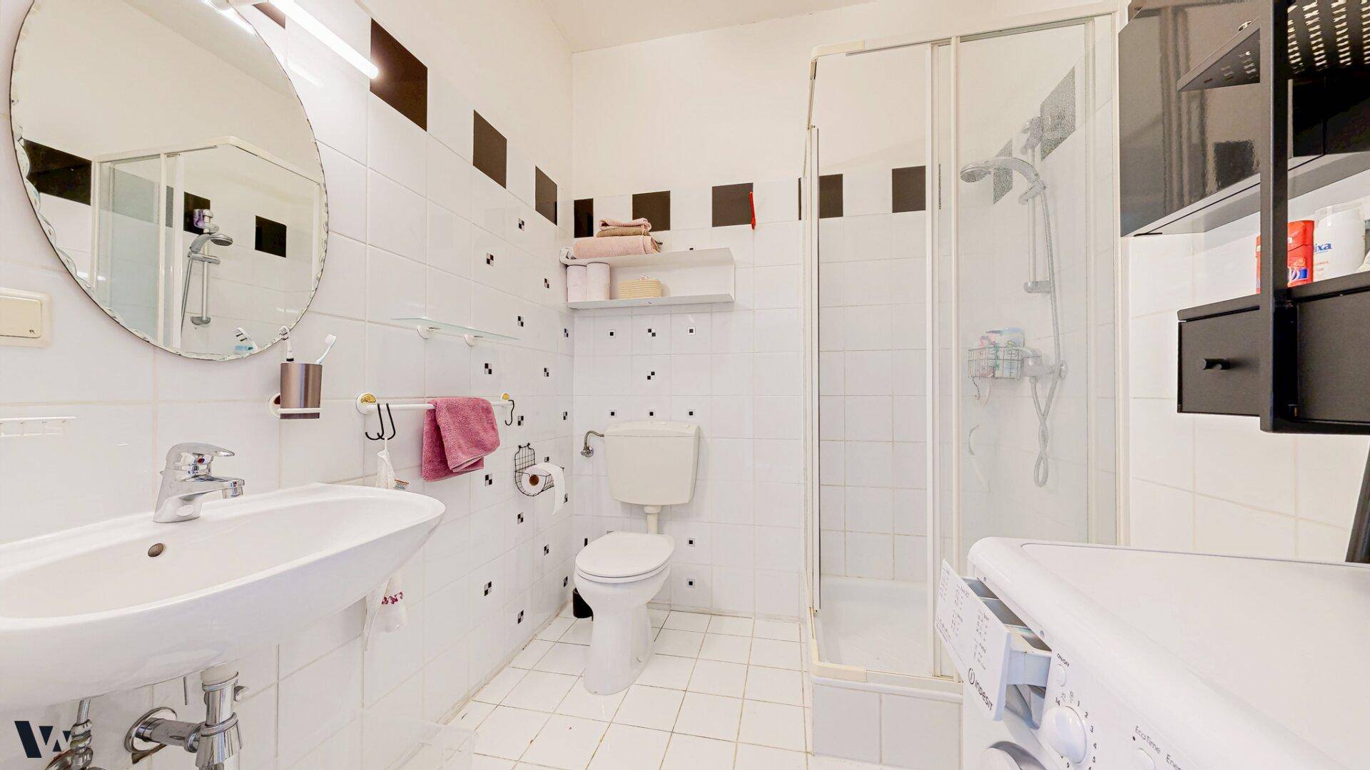 Badezimmer mit Dusche, WC und Waschmaschine, praktisch und funktional eingerichtet.