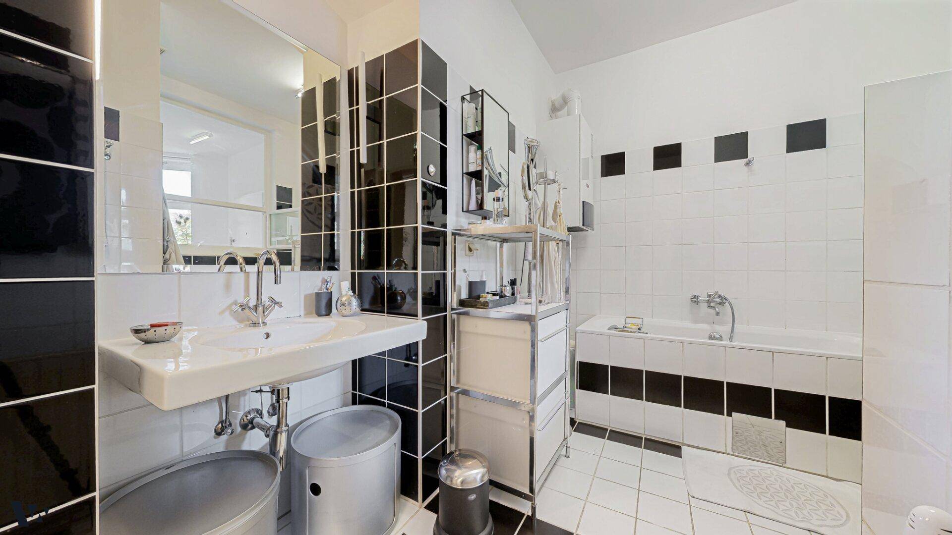 Modernes Badezimmer mit schwarz-weißen Fliesen, Badewanne und Einzelwaschbecken, stilvoll gestaltet.
