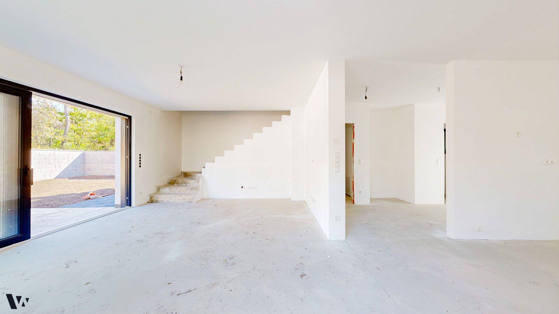 Heller, unmöblierter Wohnbereich im Rohbau mit Zugang zur Terrasse und Treppe.