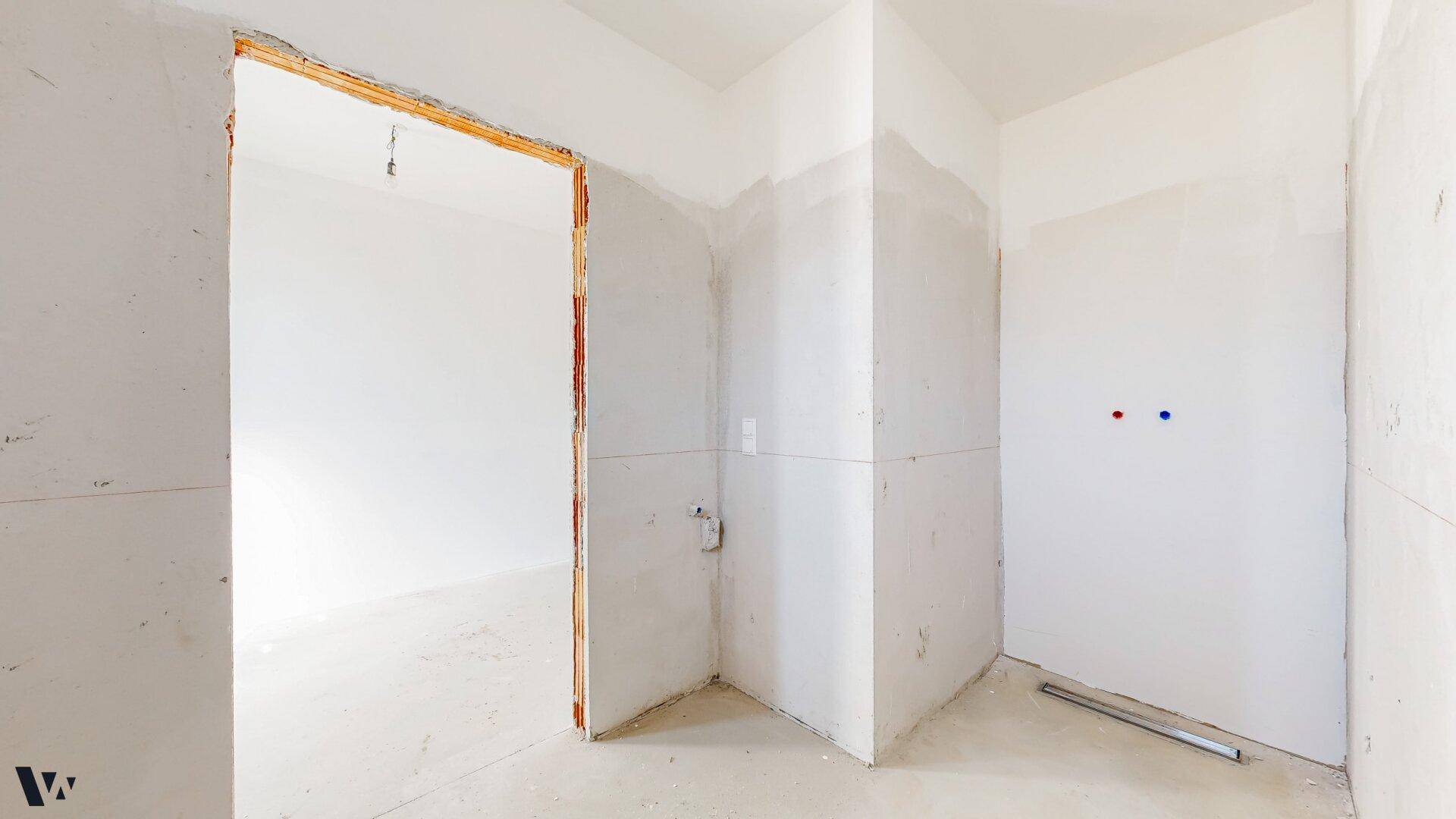 Unfertiges Badezimmer im Rohbau mit sichtbaren Wasseranschlüssen und weiß gestrichenen Wänden.