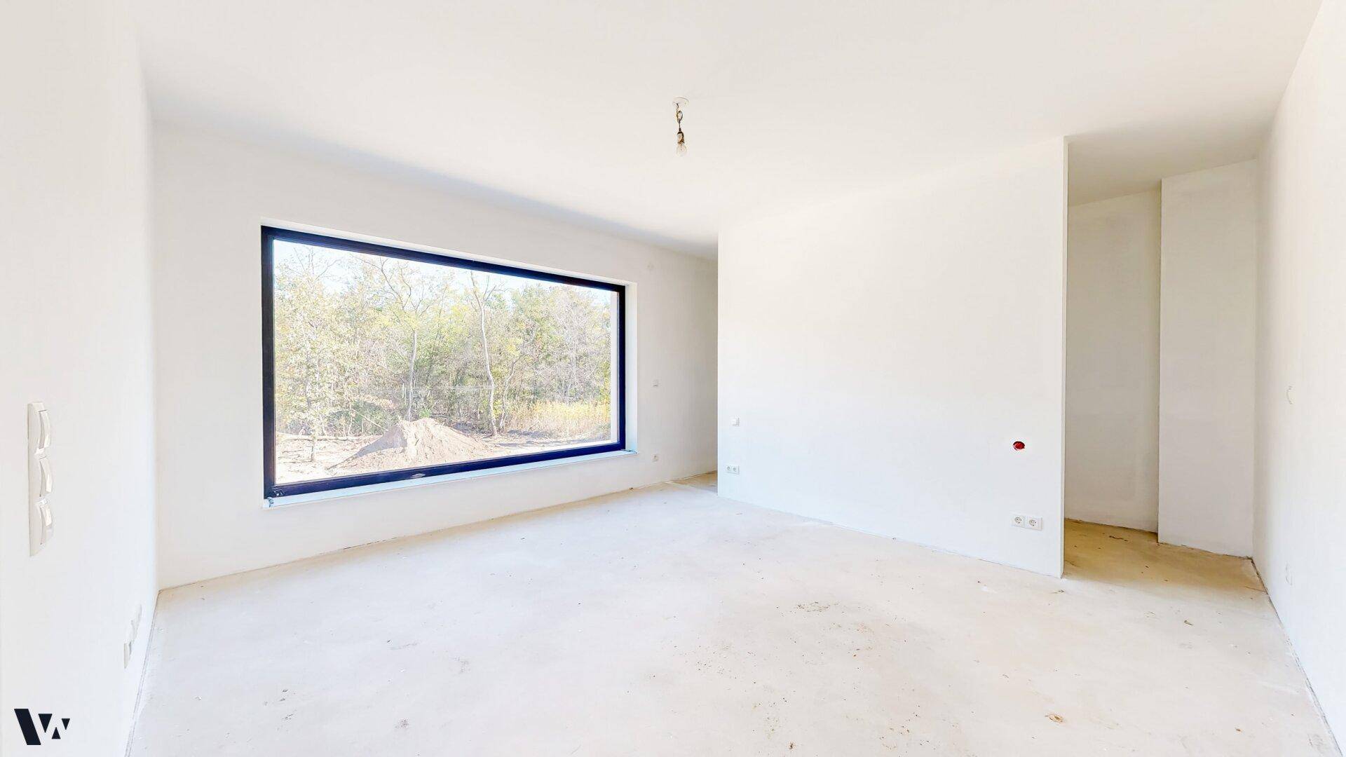 Geräumiges Zimmer im Rohbau mit großem Panoramafenster und Blick ins Grüne.