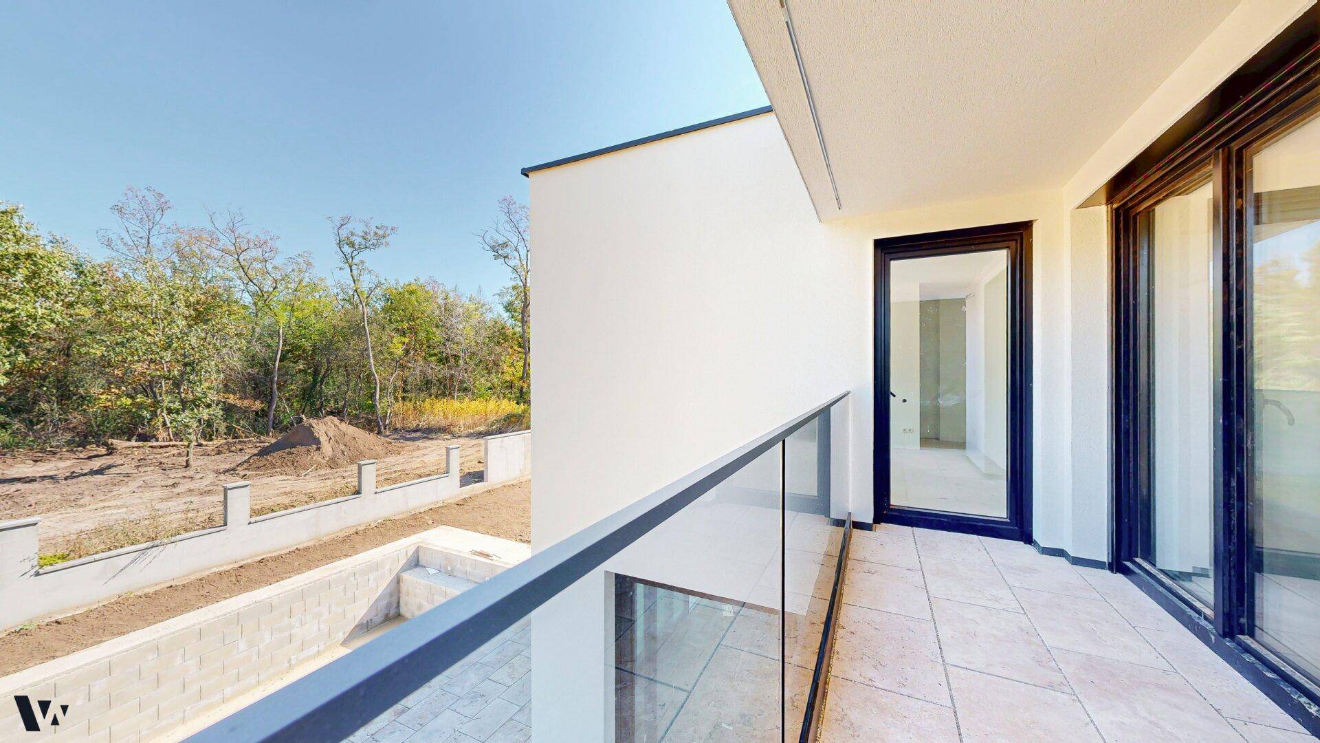Moderner Balkon mit Glasgeländer und Blick auf den Garten und die umliegende Landschaft.