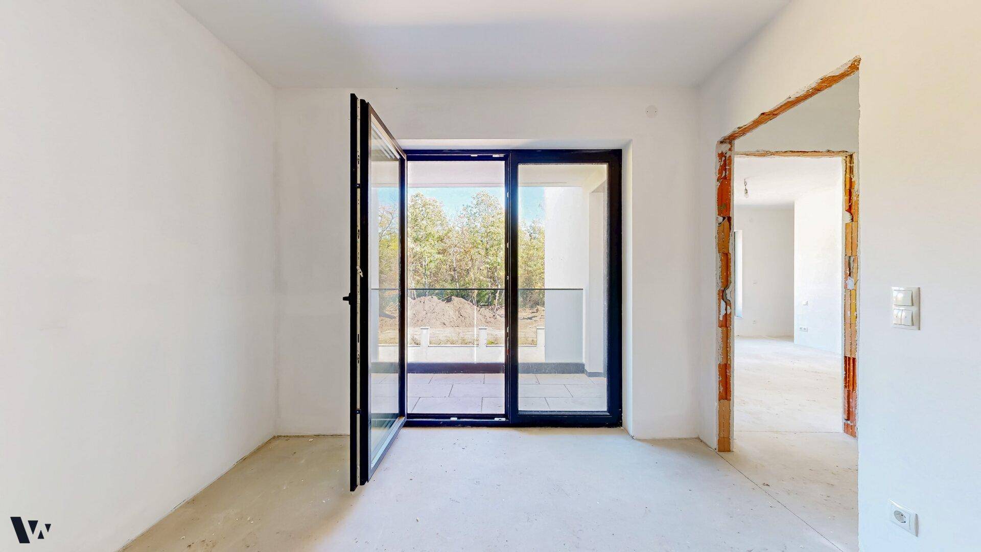 Helles Zimmer im Rohbau mit großen Fenstertüren, die zum Balkon führen und viel Tageslicht bieten.