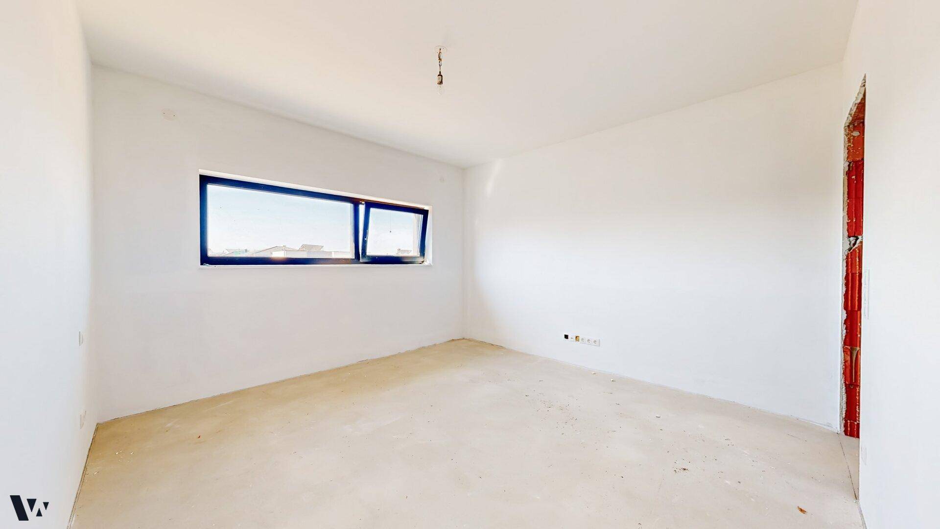 Helles Zimmer im Rohbau mit einem breiten Fenster und Blick auf die Umgebung.