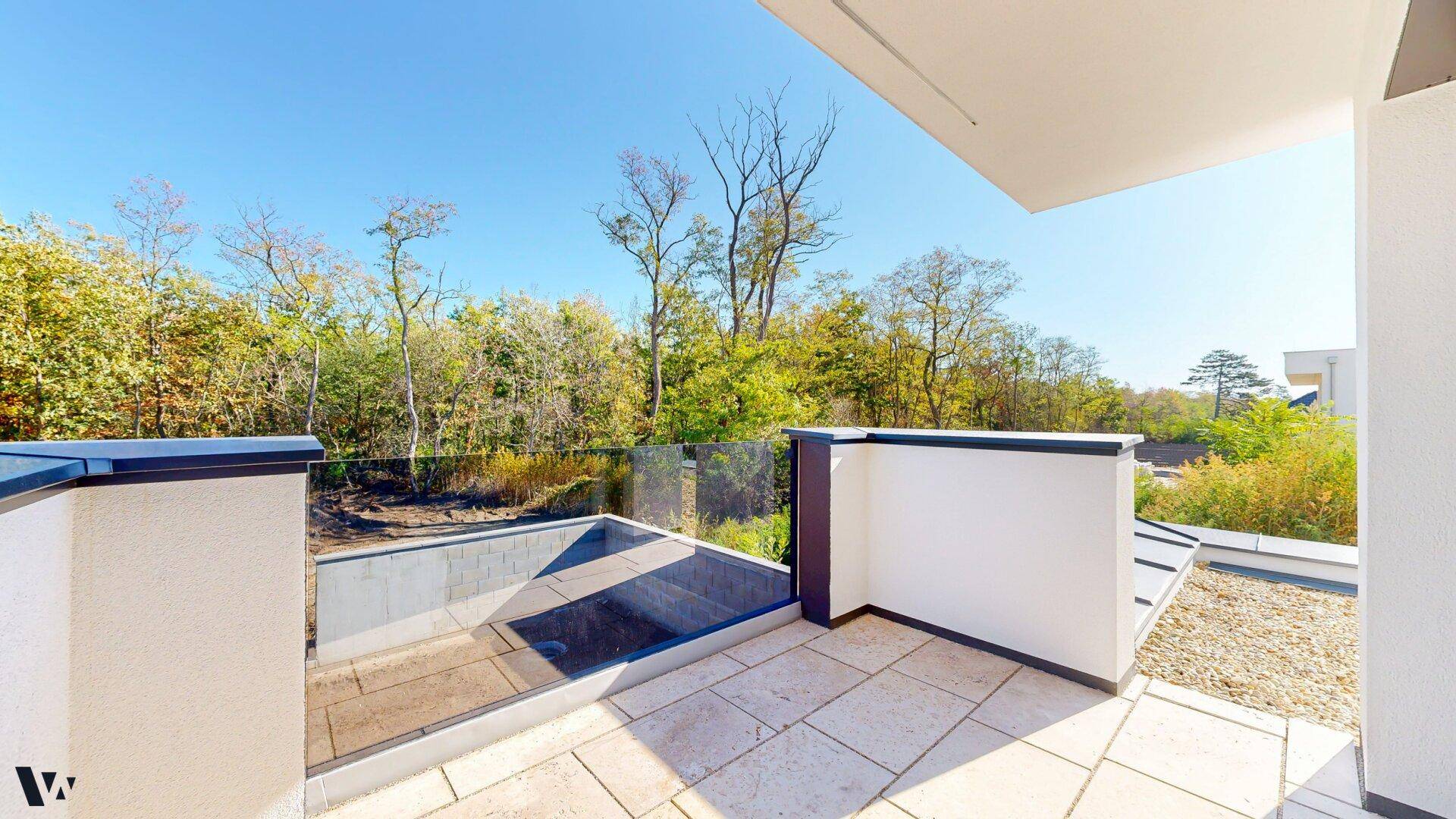 Moderner Balkon mit Glasgeländer und weitem Blick auf die grüne Umgebung und den Garten.