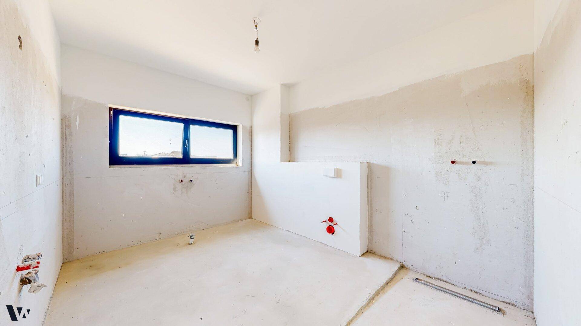 Unfertiges Badezimmer im Rohbau mit sichtbaren Wasseranschlüssen und einem Fenster.