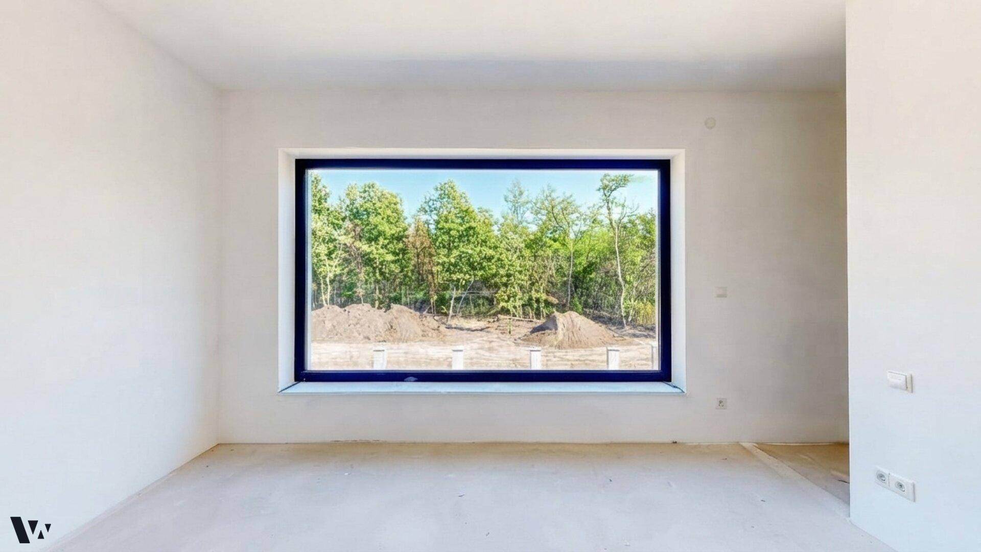 Geräumiges Zimmer im Rohbau mit breitem Fenster und weitem Blick auf die umliegende Natur.