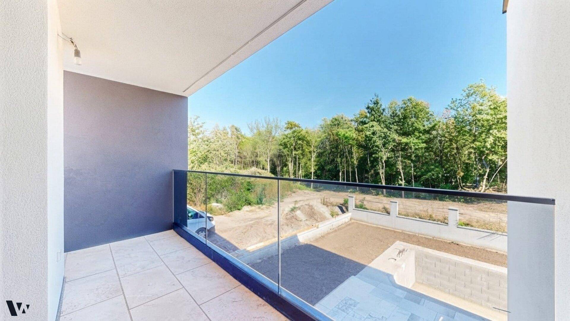 Heller Balkon mit Glasgeländer und weitem Blick auf die grüne Umgebung und den Garten.