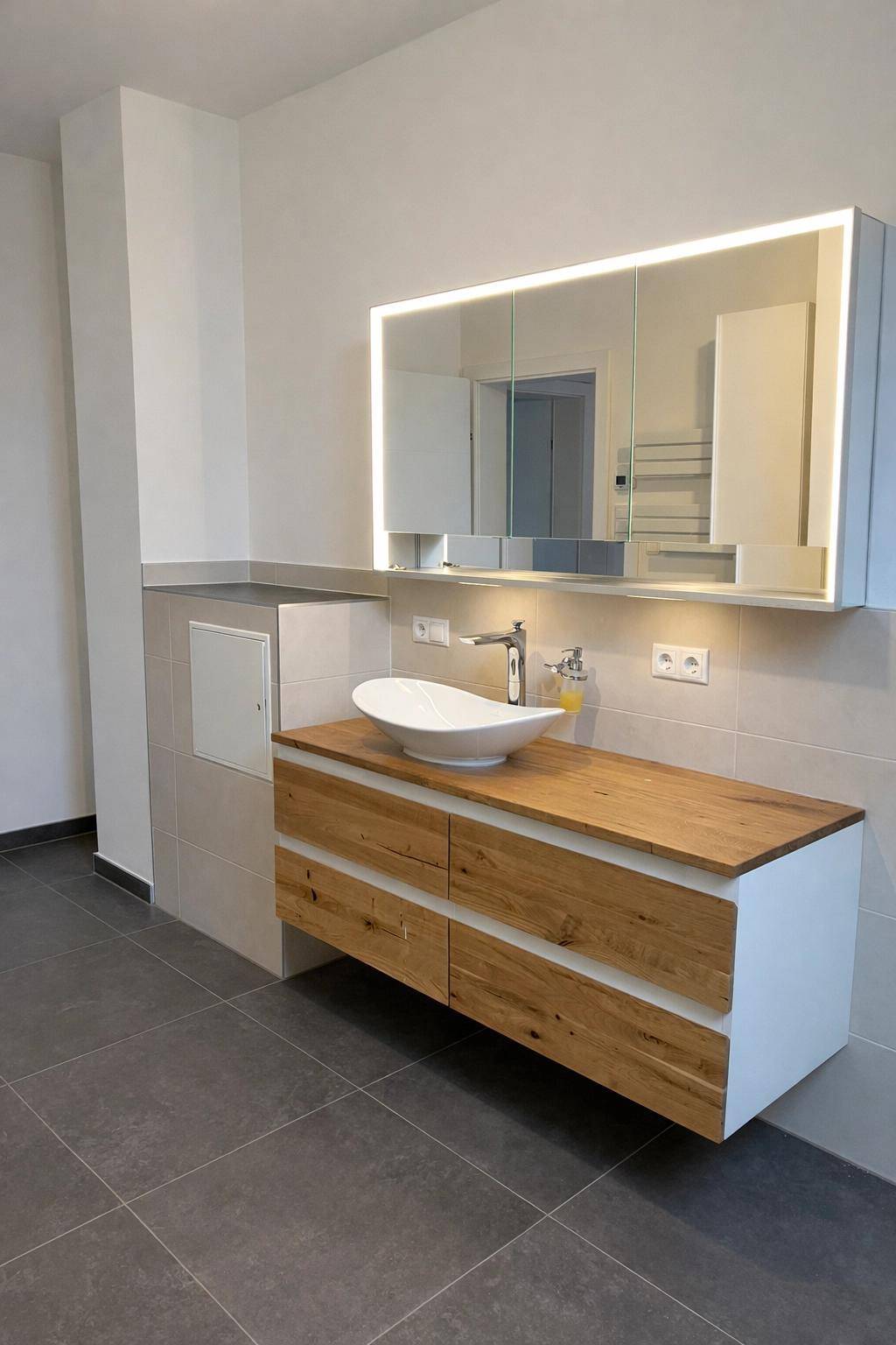 Modernes Badezimmer mit Holzwaschtisch, Aufsatzwaschbecken und beleuchtetem Spiegelschrank.