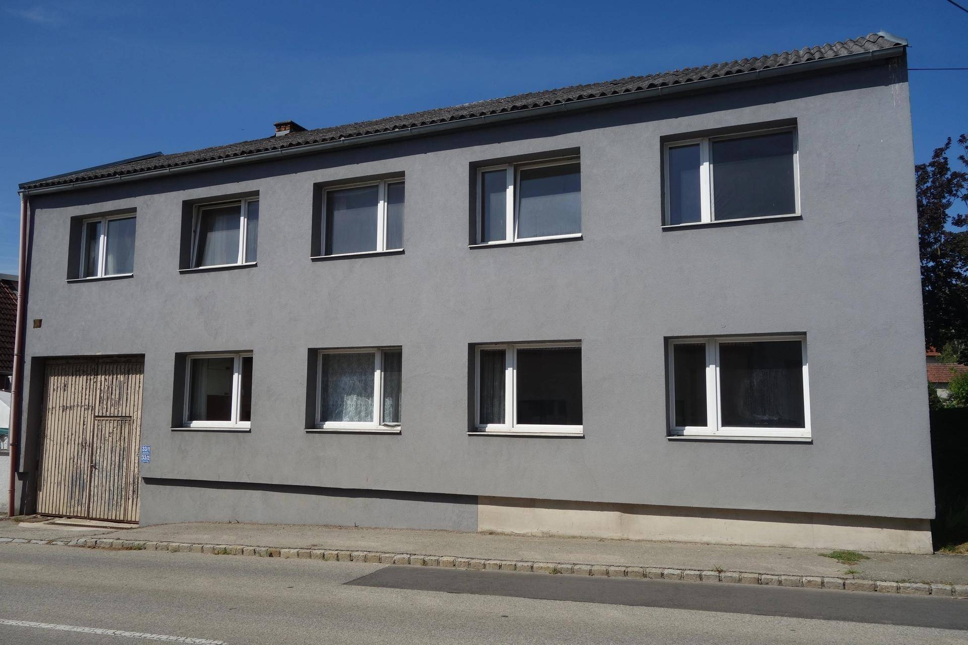 Frontansicht des zweistöckigen Gebäudes mit grauer Fassade und weißen Fenstern.