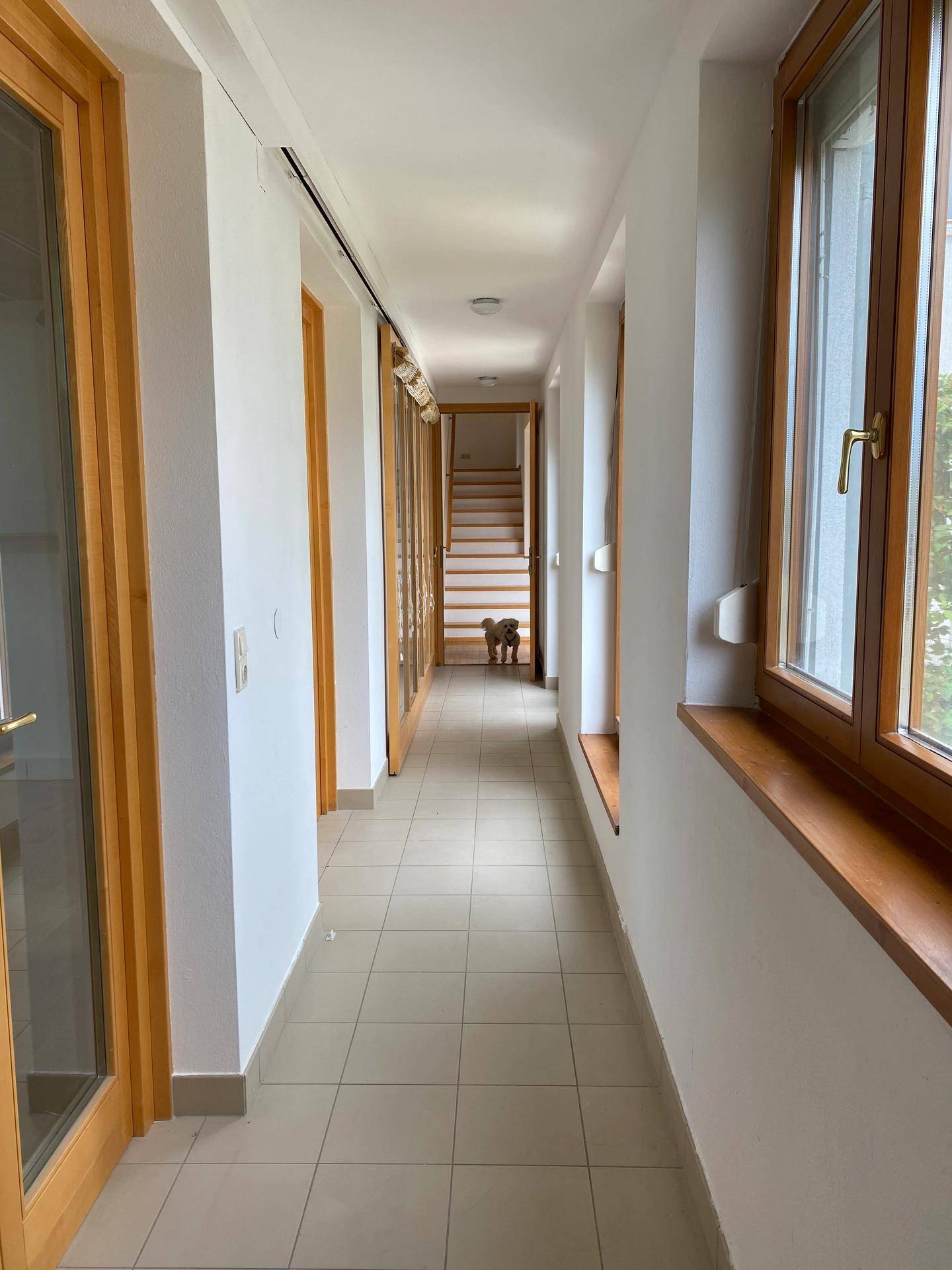 Langer, heller Flur mit Fliesenboden, Holzfenstern und Türen.