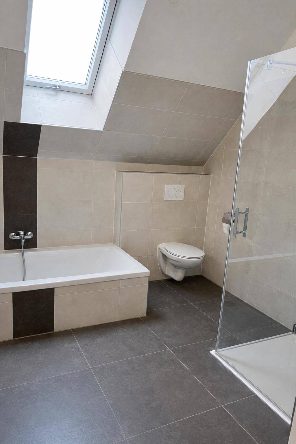 Modernes Badezimmer im Dachgeschoss mit Badewanne, Dusche, WC und Dachfenster für natürliches Licht.