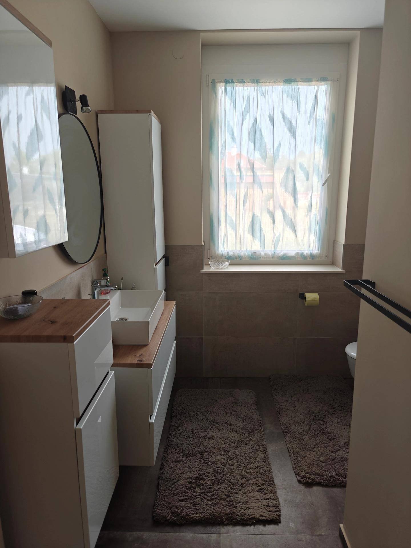Modernes Badezimmer mit Doppelwaschbecken, Spiegelschrank und Fenster für Tageslicht.