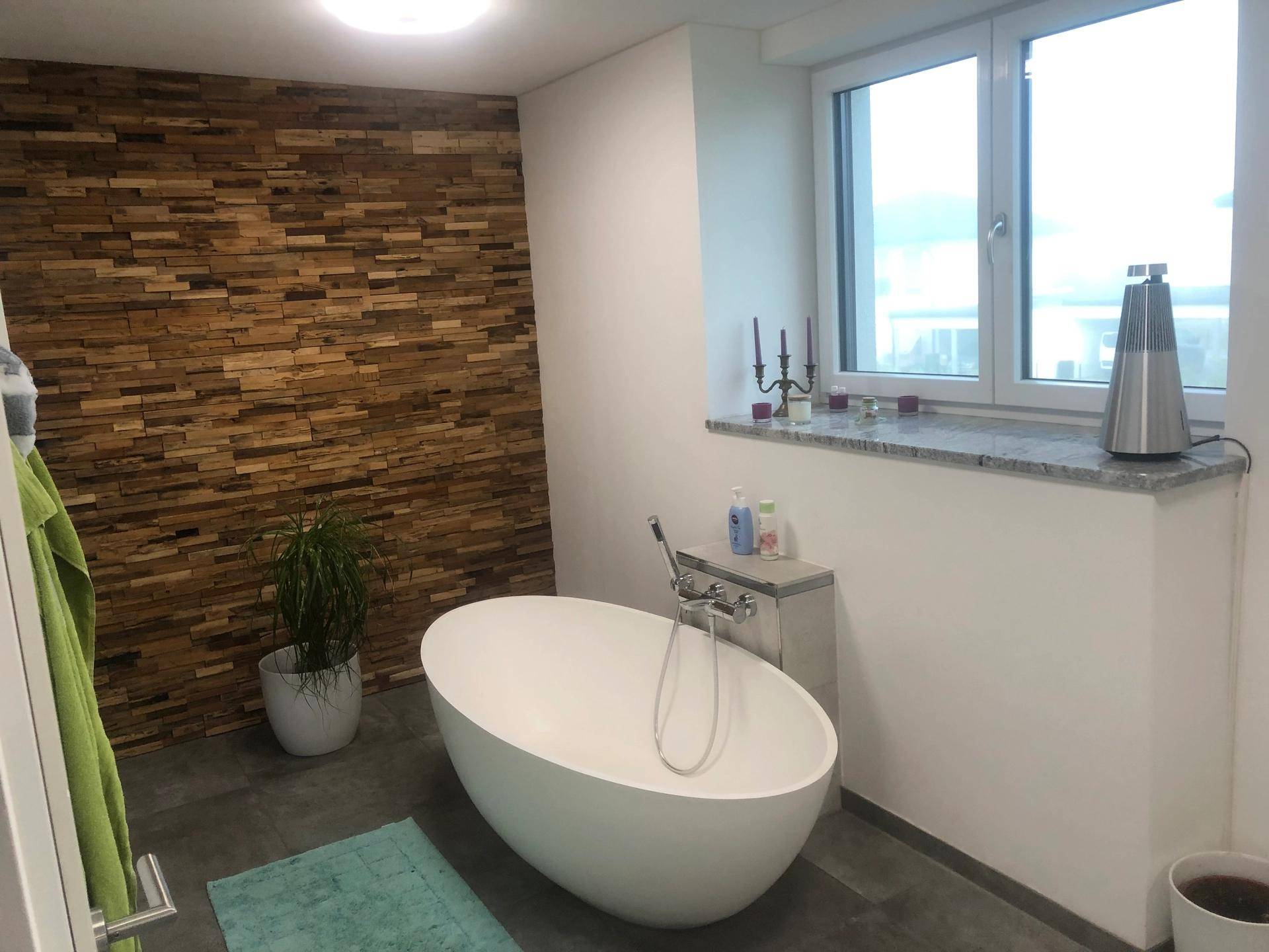 Modernes Badezimmer mit freistehender Badewanne, Holzwand und Fenster.