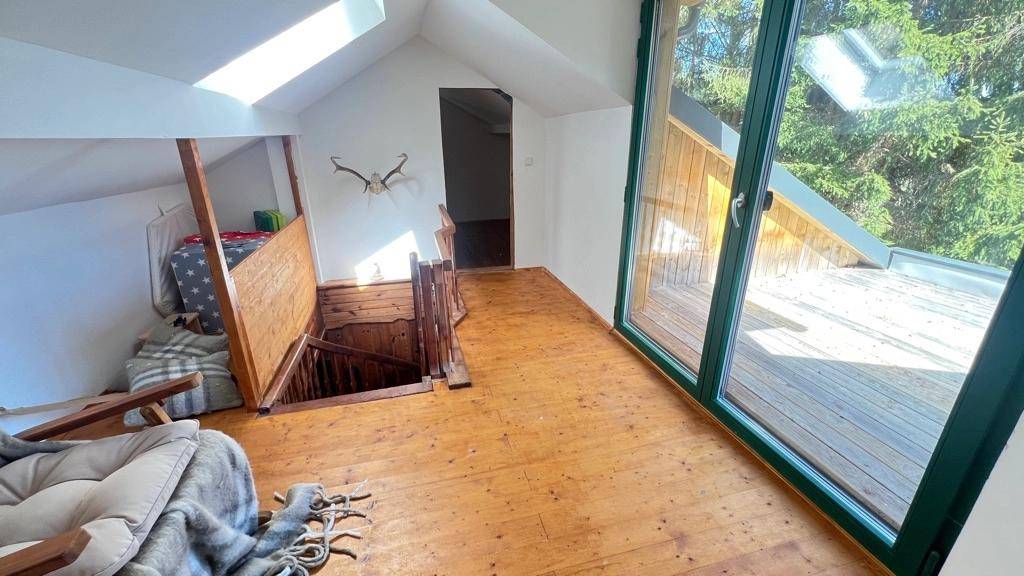 Heller Dachbodenbereich mit Holzboden, Dachfenstern und Zugang zu einem kleinen Außenbereich.