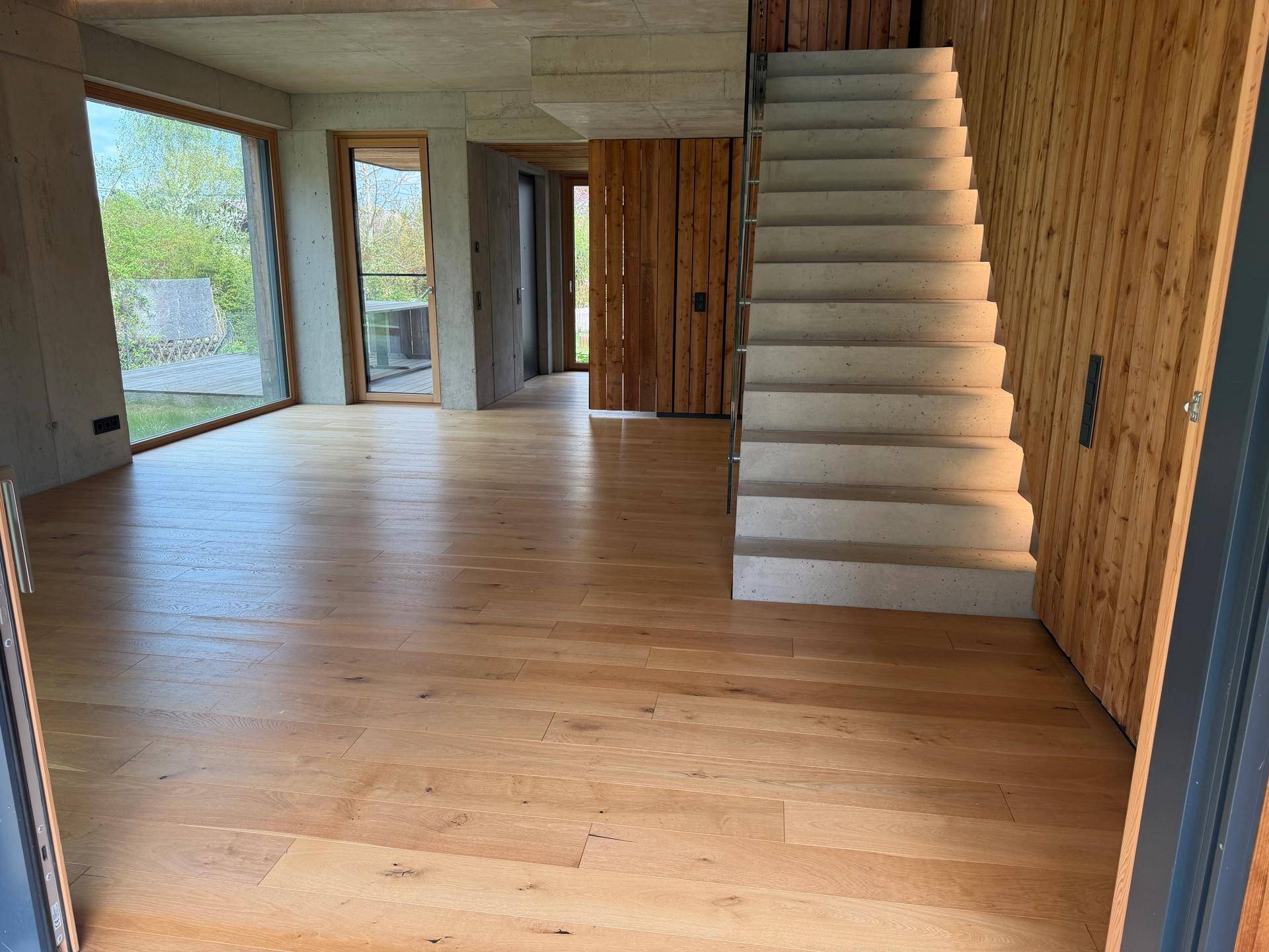 Geräumiger Wohnbereich mit Holzboden, Sichtbetondecke und einer massiven Betontreppe.