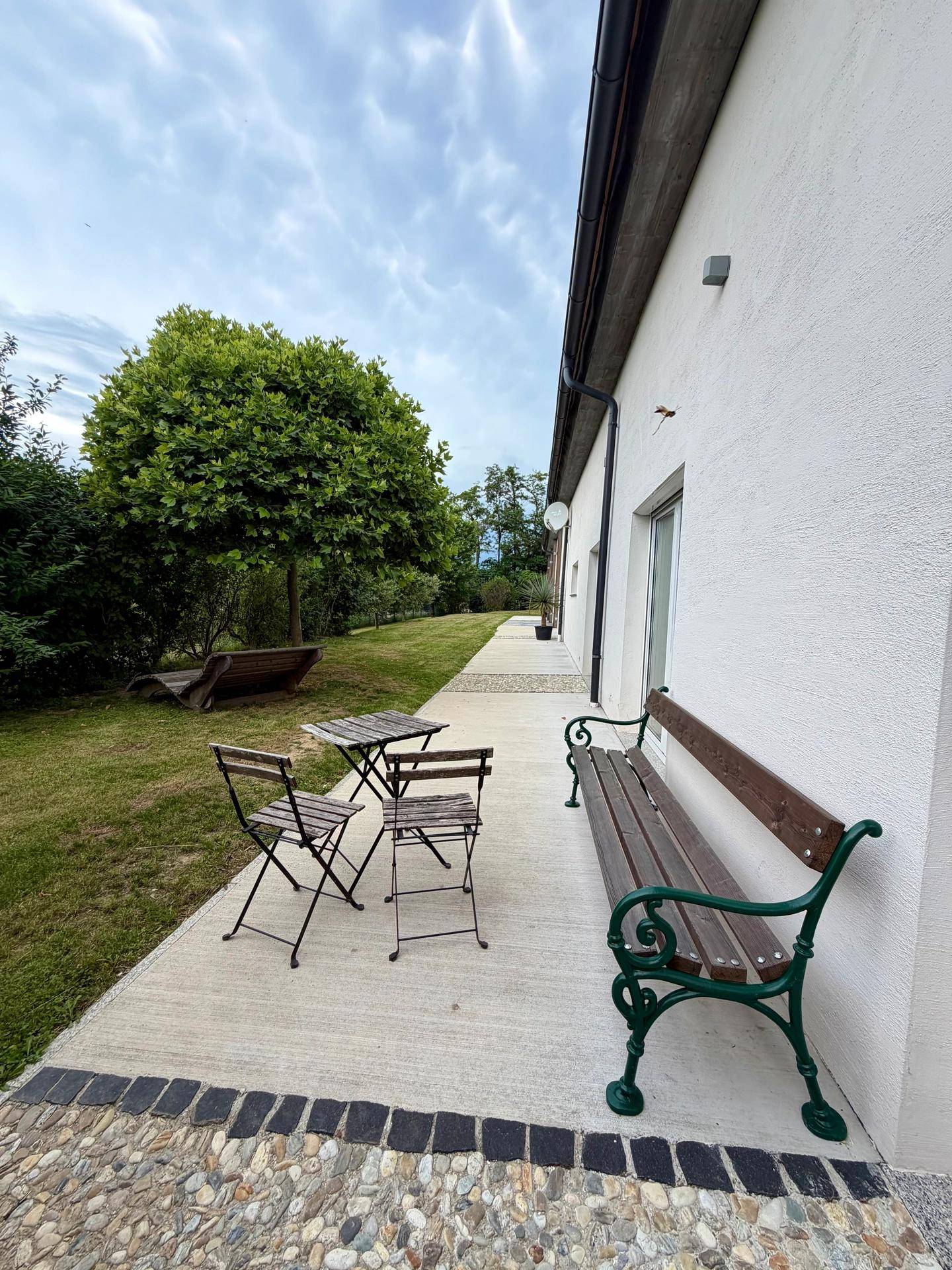 Gemütliche Terrasse am Haus mit Sitzbank und kleinem Tisch, umgeben von Grünflächen.