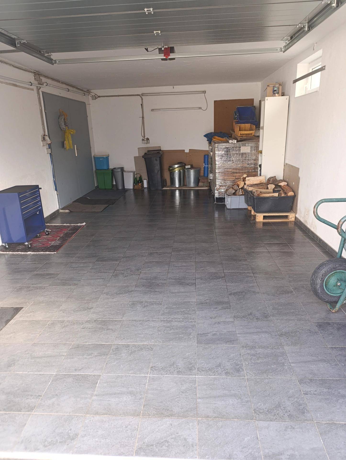 Saubere Garage mit Fliesenboden, Werkzeugen und weiteren Lagerflächen.